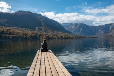 Küçük bir iskelede oturuyor ve Triglav Ulusal Parkı 'ndaki Bohinj Gölü manzarasının tadını çıkarıyor. Julian Alpleri, Slovenya