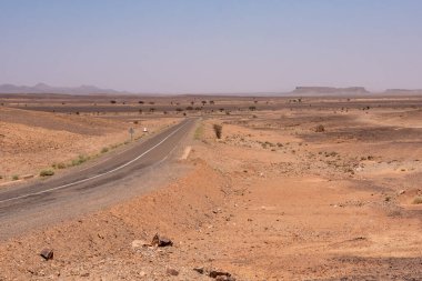 Merzouga yakınlarındaki çölden geçen bir yol. Arka planda ünlü at nalı dağı Gara Medouar, Fas.