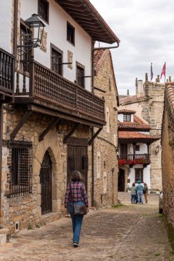 Kuzey İspanya 'nın Cantabria bölgesindeki Santillana del Mar kasabasında antik evlerle çevrili bir kaldırım taşı caddesinde bir turist.