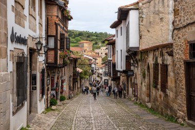 Santillana del Mar, İspanya - Mai 18, 2024 - Kuzey İspanya 'nın Santillana del Mar kasabasında antik evler ve taş bir duvarla çevrili bir kaldırım taşı caddesindeki turistler