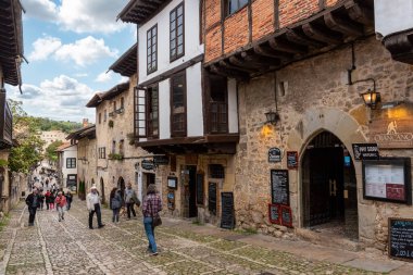 Santillana del Mar, İspanya - Mai 18, 2024 - Kuzey İspanya 'nın Santillana del Mar kasabasında antik evler ve taş bir duvarla çevrili bir kaldırım taşı caddesindeki turistler