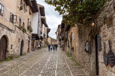 Santillana del Mar, İspanya - Mai 18, 2024 - Kuzey İspanya 'nın Santillana del Mar kasabasında antik evler ve taş bir duvarla çevrili bir kaldırım taşı caddesindeki turistler