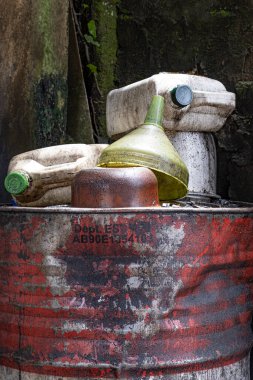 Eski ve çökmüş kırmızı ve beyaz yağ varillerinin üst kısmında boş plastik kaplar var.