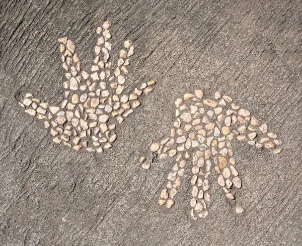 Two hand print designs made from small cream pebble stones in concrete pavement