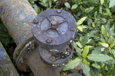 Large industrial metal pipe valve with patina color and rusted bolts