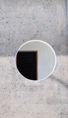 Two tone concrete wall with large circle cutout in center showing partial black door. Modern geometric design. Copy space