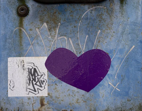 Purple heart shape on peeling blue painted metal with scratches. Grunge background texture.
