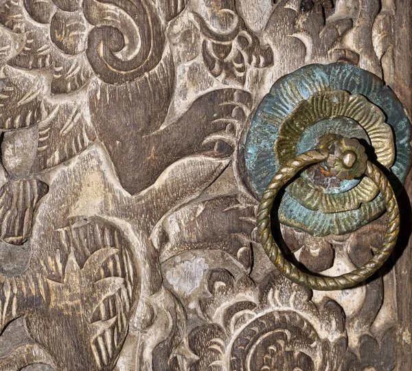Intricate wood carved door with patina round brass door knob in Bali, Indonesia