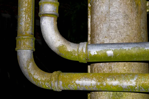 Mold covered industrial steel water pipes with elbows against rusty metal box