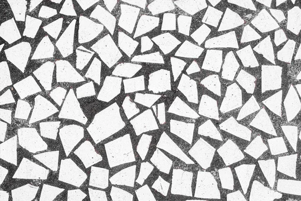 Broken white porcelain tile pieces set in black concrete sidewalk in Bali, Indonesia. Background texture