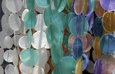 Pastel rengi yuvarlak şeffaf madalyon şeklinde deniz kabukları iple sarkıyor.