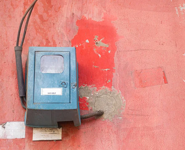 Old blue electrical box on a red painted concrete wall with chipped paint and black wires hanging. Copy space