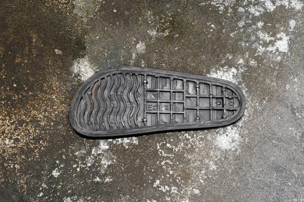 Black rubber sole with treading laying against dirty concrete pavement. Copy space