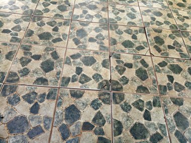 Bahçe zemininin beyaz ve koyu yeşil soyut bir motifi var. Birkaç tarafı çatlamış.