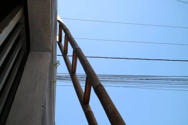 Bir evin duvarına dayanmış bir bambu merdiveni fotoğrafı, gün boyunca, aşağıdan çekilmiş.