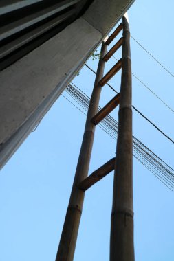 Bir evin duvarına dayanmış bir bambu merdiveni fotoğrafı, gün boyunca, aşağıdan çekilmiş.