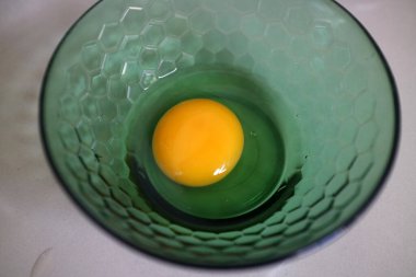 Tek bir çiğ yumurta, yeşil desenli bir kasede düzgünce duruyor.