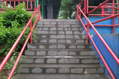 Yeşil ve mavi renkli duvarlarla çevrili halka açık bir alanda, kırmızı metal tırabzanları ve ıslak merdivenleri olan beton bir merdivenin ön görüntüsü.