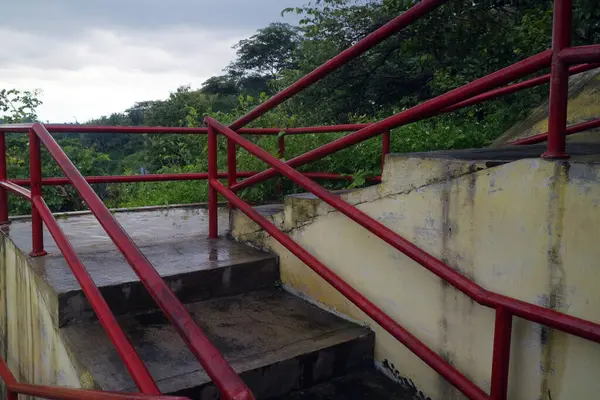 Yağmurdan kısa bir süre sonra çekilen parlak kırmızı metal tırabzanlarla ıslak beton merdivenlerin fotoğrafı.
