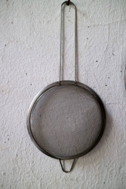 Uzun saplı bir mutfak ağı süzgeci dokulu duvarda asılı.