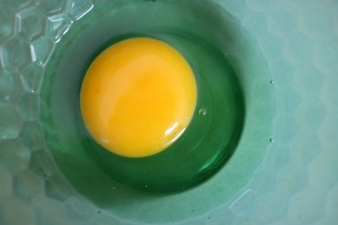 Yeşil bir kasenin içinde parlak sarı sarısı olan çiğ bir yumurta.