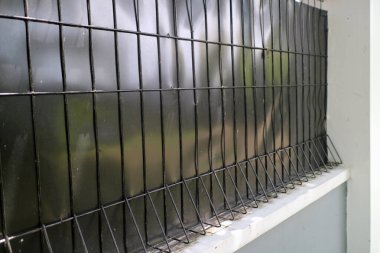 Dibinde keskin, açılı çiviler olan, ızgara desenli siyah metal bir çitin yakın görüntüsü. Arka plan bulanık. Bahçe ya da açık alan olabilir..