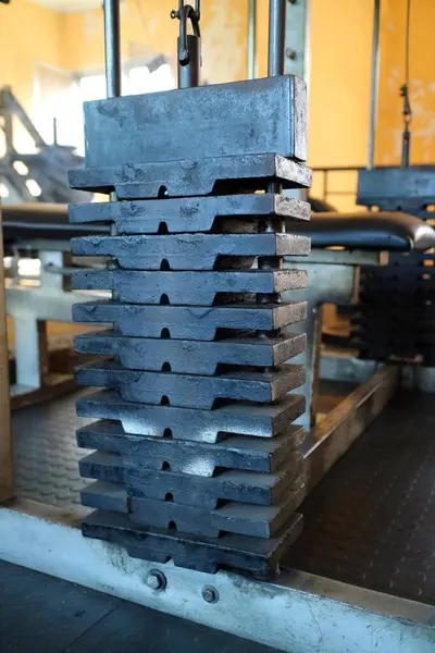 Spor salonundaki ağırlık plakalarının yakın çekim görüntüsü tabakaların dokusunu ve yapısını gözler önüne seriyor. Arka planda spor aletleri ve turuncu bir duvar var..