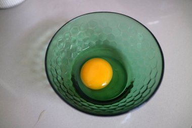 Altıgen desenli yeşil cam bir kasede tek bir çiğ yumurta sarısı..