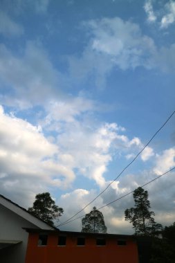 Bir bina ve ağaçların üzerinde dağınık bulutlarla huzurlu bir gökyüzü..