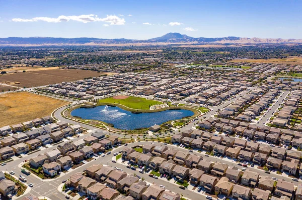 An aerial photo over a community in Oakley, California with a man made lake in the foreground and mountain with a blue sky in the background with room for text