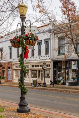 Downtown Oroville light post decorated in a Christmas themed wreath and planter boxes with businesses and a clock tower in the background