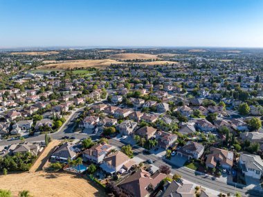 Drone over a suburban neighborhood in Antioch, California with homes, pools, streets, trees, solar and a blue sky clipart