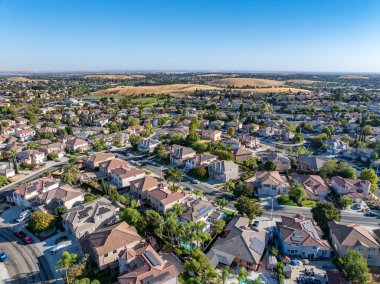 Drone over a suburban neighborhood in Antioch, California with homes, pools, streets, trees, solar and a blue sky clipart