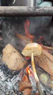 Sivri uçlu bir sopayla ekmek kızartırken, su da kamp ateşinde çay içmek için su kaynatıyor. Huzurlu bir ormanda kırsal yemek pişirme.