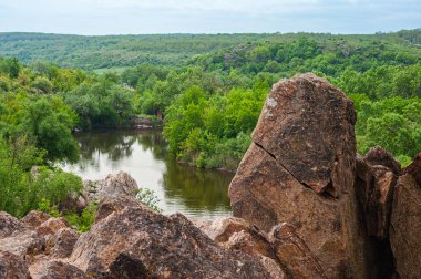 Çarpıcı bir kayalık tepe, gür bir ormanlık nehir kıyısı üzerinde yükselir. Dokulu yüzeyi ve doğal ışıkla vurgulanan çarpıcı bir rahatlama. Akan nehir manzaraya derinlik katar..