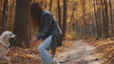 Genç neşeli kızıl saçlı kız sonbahar ormanlarında Labrador av köpeğiyle gezip oynuyor.