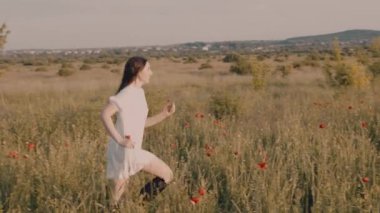 Genç ve çekici bir kadın gelincik tarlasında günbatımının tadını çıkarıyor.