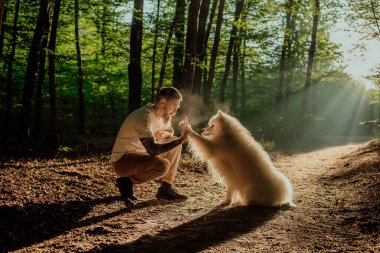 Gündoğumunda ormanda kollarında dövmeleri olan ve sevimli ve tüylü köpeğiyle oynayan bin yıllık hippi erkek.