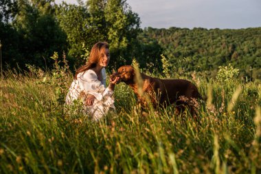 Güzel kırsal alanda köpeğiyle oynayan neşeli genç bir kadın. Kadın ve sırtında köpek yürüyor ve eğleniyor.