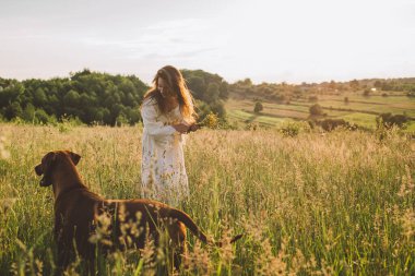 Güzel kırsal alanda köpeğiyle oynayan neşeli genç bir kadın. Kadın ve sırtında köpek yürüyor ve eğleniyor.