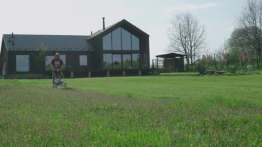Adamın biri kır evindeki bahçesinde çimleri biçiyor.