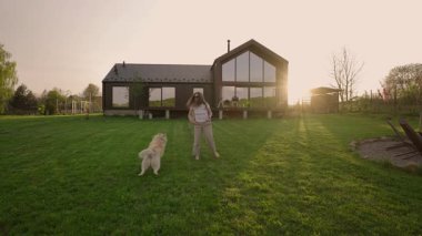 Günbatımında kırsalda yeni biçilmiş bir çimenlikte Sibirya köpeğiyle oynayan bir kadın.