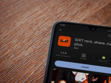 Lod, Israel - July 16,2023: SIXT rent app play store page on smartphone on wooden background. Top view flat lay with copy space.