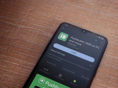 Lod, Israel - July 16,2023: Pushbullet app play store page on smartphone on wooden background. Top view flat lay with copy space.