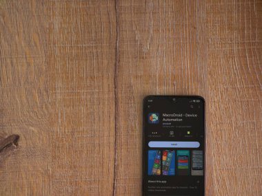 Lod, Israel - July 16,2023: MacroDroid app play store page on smartphone on wooden background. Top view flat lay with copy space.