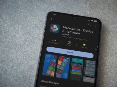 Lod, Israel - July 16,2023: MacroDroid app play store page on smartphone on ceramic stone background. Top view flat lay with copy space.