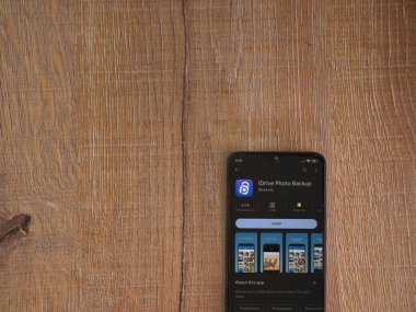 Lod, Israel - July 16,2023: IDrive Photo Backup app play store page on smartphone on wooden background. Top view flat lay with copy space.