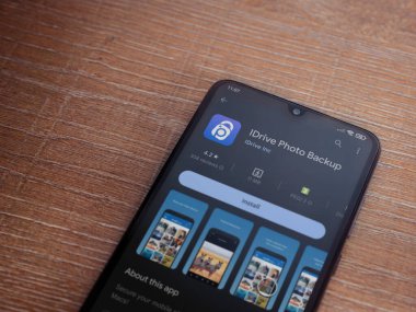 Lod, Israel - July 16,2023: IDrive Photo Backup app play store page on smartphone on wooden background. Top view flat lay with copy space.