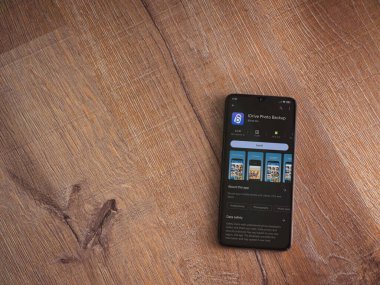 Lod, Israel - July 16,2023: IDrive Photo Backup app play store page on smartphone on wooden background. Top view flat lay with copy space.