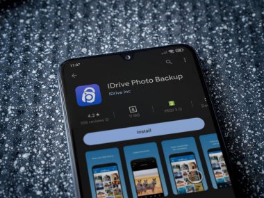 Lod, Israel - July 16,2023: IDrive Photo Backup app play store page on smartphone on a metallic background. Close up top view flat lay.